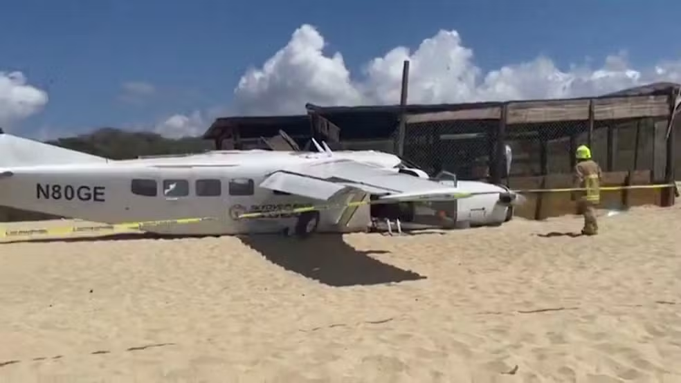 Uma pessoa fica perto dos destroços de um pequeno avião de paraquedista que caiu na praia de Bacocho, no estado de Oaxaca, México — Foto: Puerto Global/Folheto via REUTERS